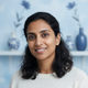 Portrait headshot of a smiling person, conveying happiness and trust, against a soft sky blue and white background.