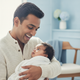 Close-up portrait of a happy, smiling parent holding a baby, in a soft, naturally lit setting with a blue and white backgroun